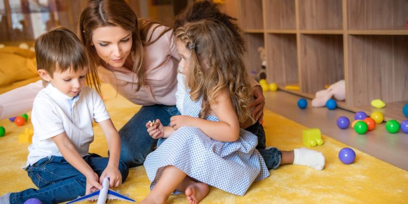 tutor-hugging-adorable-kids-on-carpet-in-kindergarten-1.jpg